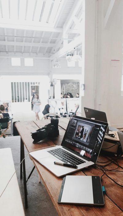 A bright, modern workspace featuring laptops, a camera, and a drawing tablet in an indoor office.